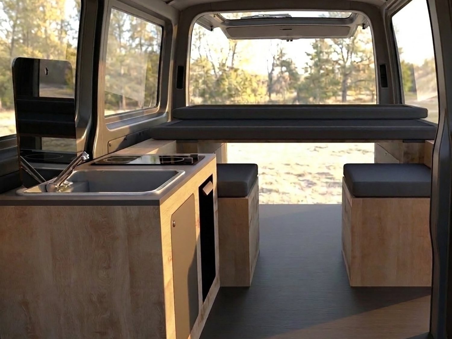 Campervan interior with birch plywood kitchen module, sink and hob, bench seating and the rear doors open onto woodland